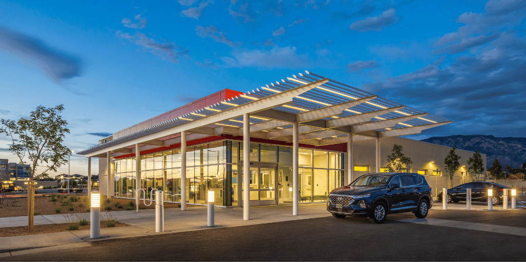 A lit up building outside at dusk with two cars in front