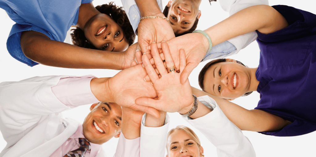 Five healthcare workers huddled together with hands in the middle
