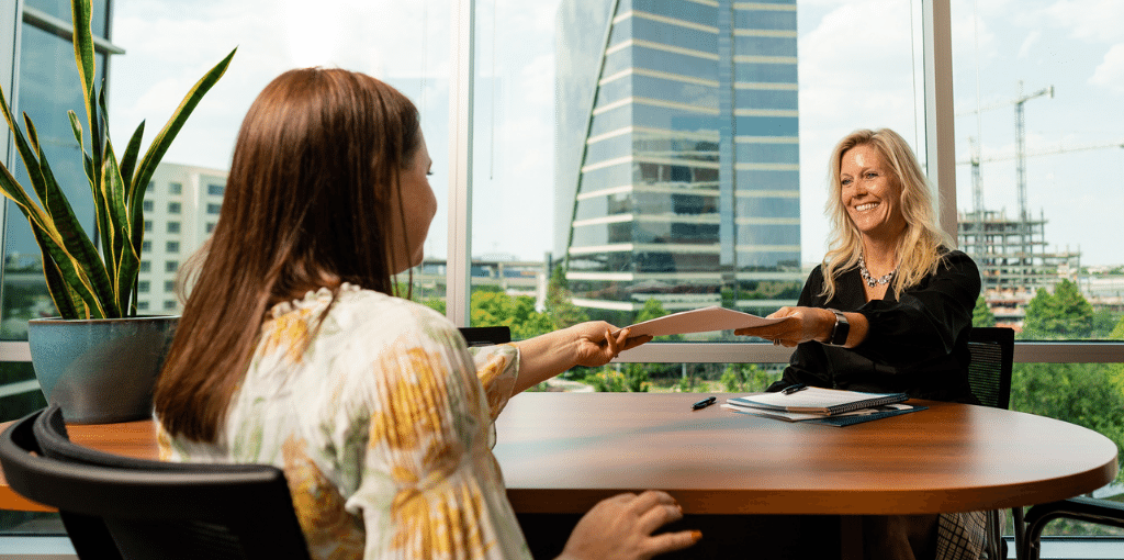 woman passing a folder to a younger woman